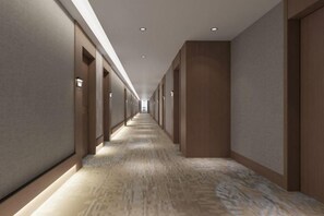 A long, narrow hotel corridor with doors on both sides and a carpeted floor.