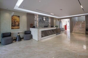 A modern lobby with a reception desk, seating area, and a staircase.