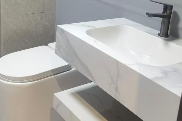 A bathroom with a white toilet, a marble sink, and a modern faucet.
