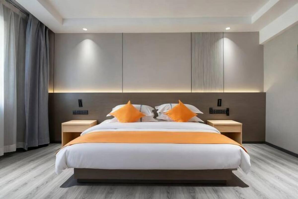 A modern hotel room with a large bed, two nightstands, and a headboard with built-in lighting.