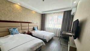 Habitación de hotel con dos camas, un escritorio, una silla, un televisor y una ventana con cortinas.