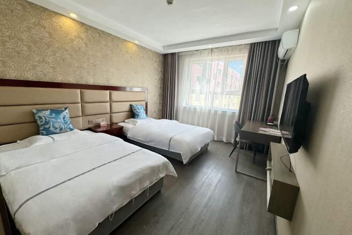Une chambre d’hôtel avec deux lits, un bureau, une chaise, une télévision et une fenêtre avec des rideaux.