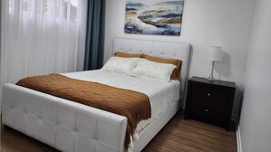 Ein Schlafzimmer mit Bett, Nachttisch, einem Gemälde und einem Fenster mit Vorhängen.