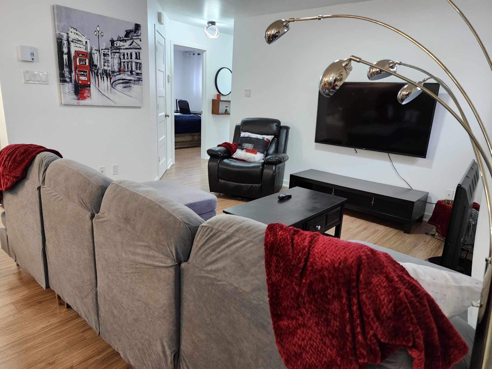 Una sala de estar moderna con un sofá gris, un sillón negro, un televisor de pantalla plana y una lámpara de pie.