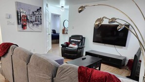 Ein modernes Wohnzimmer mit einem grauen Sofa, einem schwarzen Sessel, einem Flachbildfernseher und einer Stehlampe.