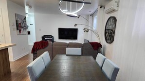 Ein modernes Wohnzimmer mit Esstisch, Sofas, Fernseher und einer großen Uhr an der Wand.