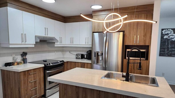 Eine moderne Küche mit weißen Schränken, einem Edelstahlkühlschrank, einem eingebauten Backofen und einer Holzinsel mit Spüle.