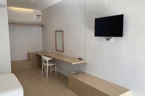 Une chambre d’hôtel moderne équipée d’un lit, d’un bureau, d’une chaise, d’un tél éviseur fixé au mur et d’une petite étagère.