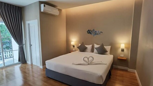 Une chambre d’hôtel avec un grand lit, deux lampes de chevet, un climatiseur fixé au mur et une vue sur l’extérieur grâce à une porte coulissante.