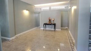Un hall d’entrée spacieux, doté d’un sol carrelé, d’une petite table avec une lampe et d’un escalier en arrière-plan.