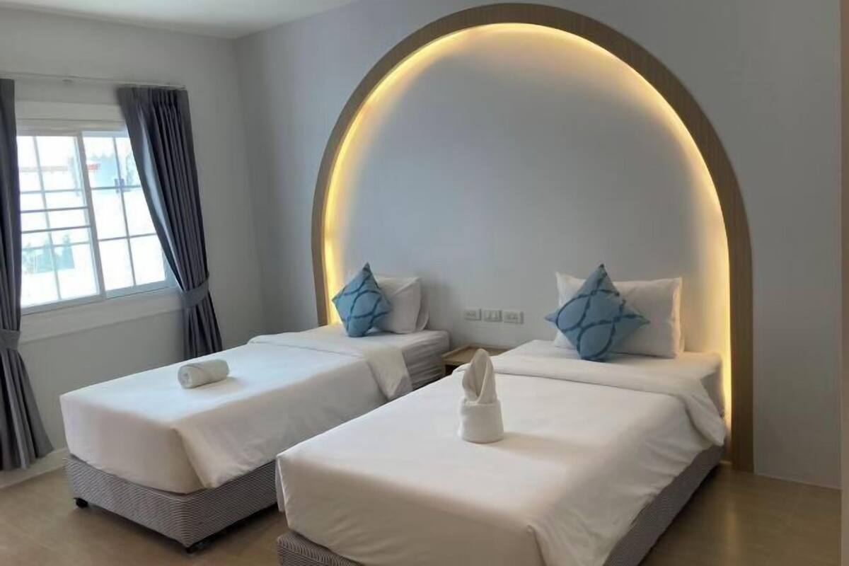 Hotellihuone, jossa on kaksi sänkyä, suuri kaareva ikkuna ja moderni sisustus.