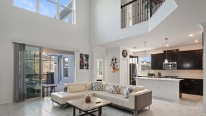 A spacious living area with a large sofa, a coffee table, and a kitchen in the background. - Large 5BR Home w Pool, Princess Room, Resort Access (Kissimmee)