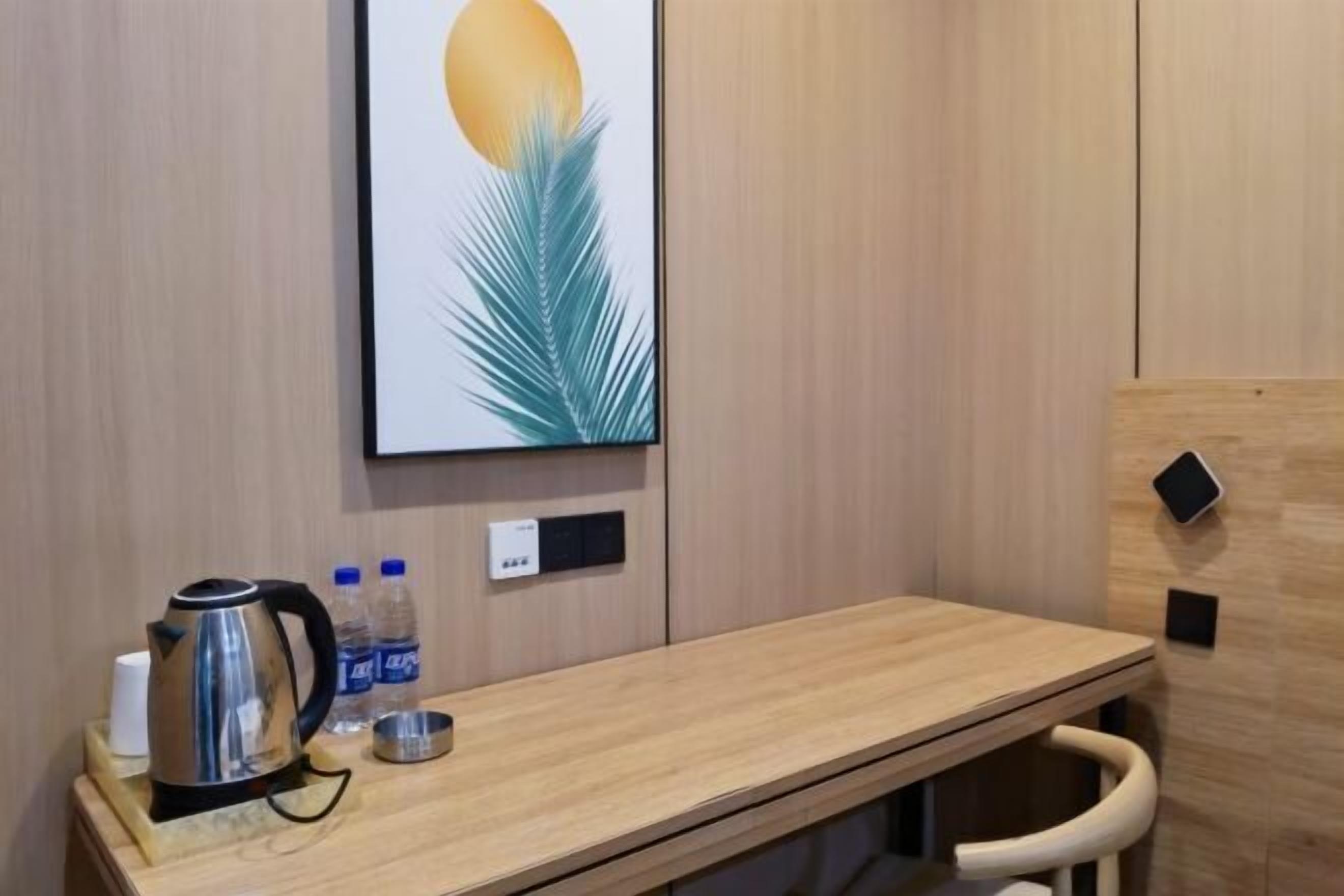 A hotel room with a wooden desk, a framed picture on the wall, a kettle, water bottles, and a small tray.