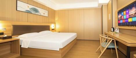 A hotel room with a bed, bedside table, desk, chair, and a large digital screen on the wall.