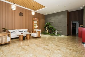 A hotel lobby with a wooden reception desk, a sofa set, a coffee table, and a small indoor garden. - Shankee Hotel (Nanchang Chengbihu Park) (Nanchang County)