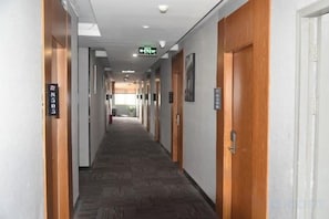 A hotel corridor with wooden doors, a carpeted floor, and emergency exit signage. - Shankee Hotel (Nanchang Chengbihu Park) (Nanchang County)