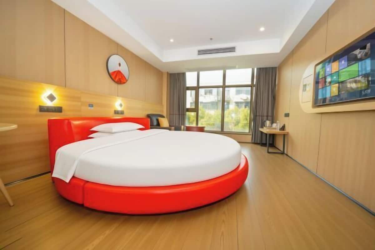 Een moderne hotelkamer met een rond bed, houten paneelwanden, een groot raam en een tv aan de muur.