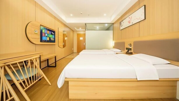 A hotel room with a wooden floor, a bed with white bedding, a desk with a chair, a television mounted on the wall, and a framed picture above the bed. - Shankee Hotel (Nanchang Chengbihu Park) (Nanchang County)
