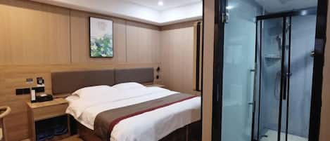 A hotel room with a bed, bedside table, and a glass-enclosed shower area.