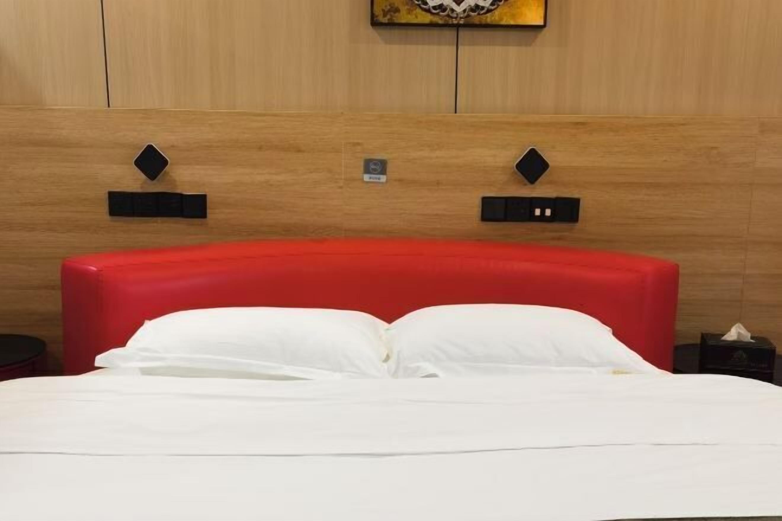 A neatly made bed with white linens and a red headboard in a hotel room.