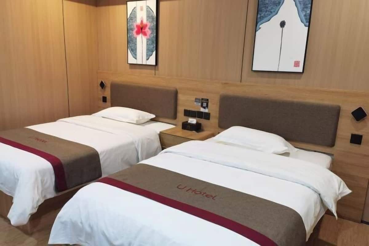 Een hotelkamer met twee bedden, elk met hoofdbord, nachtkastje en een kunstwerk aan de muur.