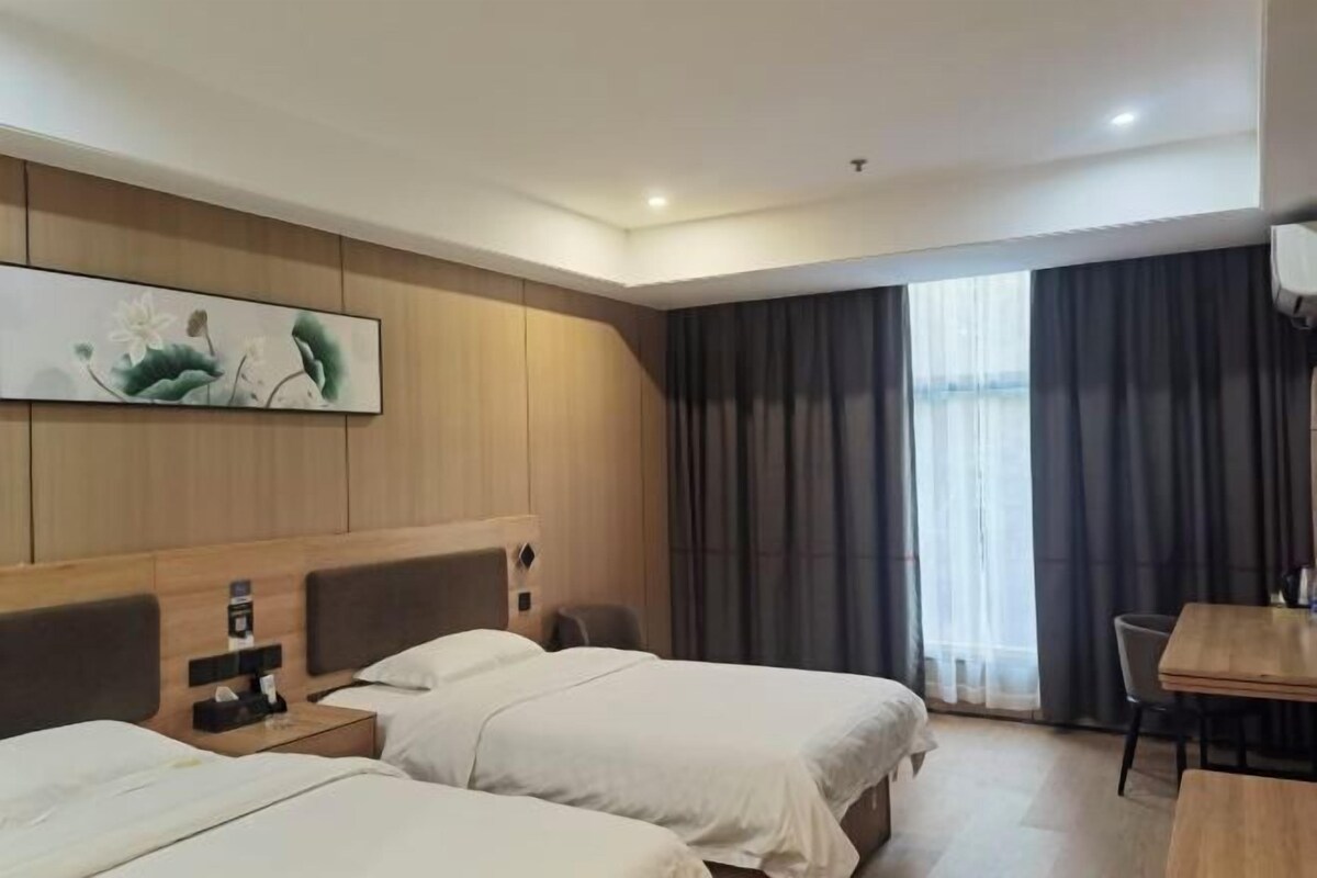 A hotel room with two beds, a wooden headboard, a painting, a desk, and a window with curtains.