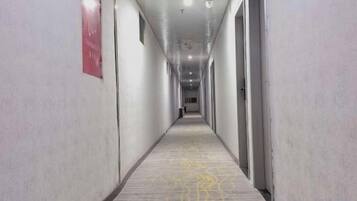 Un pasillo largo y estrecho con alfombra estampada, puertas a ambos lados y un letrero rojo en la pared izquierda.