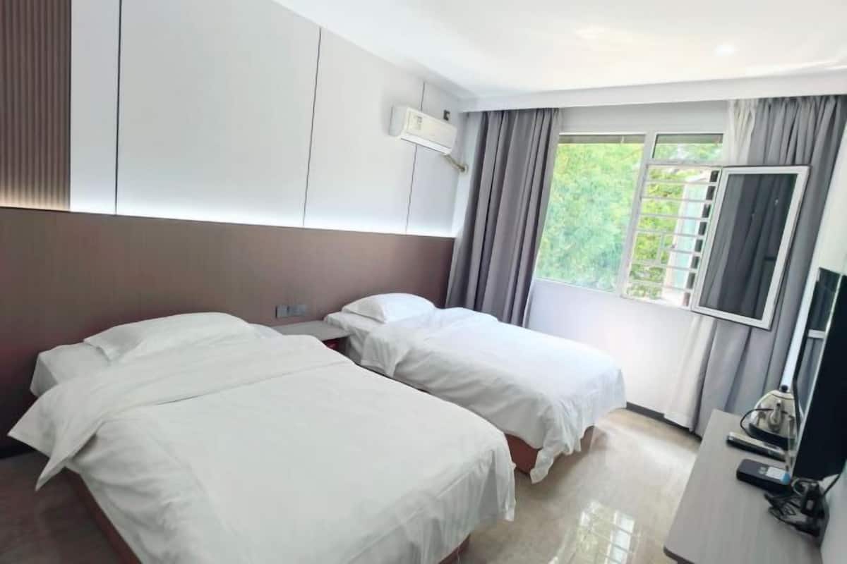 A hotel room with two beds, a TV, a desk, and a window with curtains.
