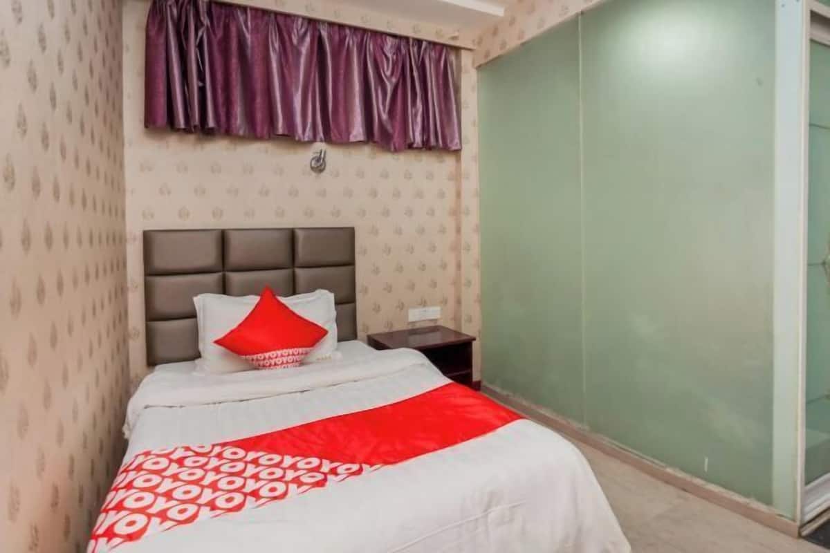 A hotel room with a bed, a nightstand, a window with a curtain, and a wall with a patterned wallpaper.