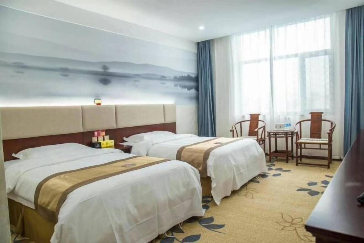 Une chambre d’hôtel avec deux lits, un bureau, des chaises et une grande fenêtre avec des rideaux.