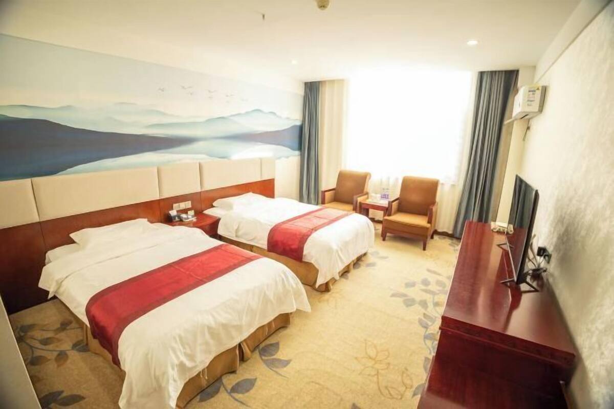 Une chambre d’hôtel avec deux lits, un bureau, une chaise, une télévision et un tableau au mur.