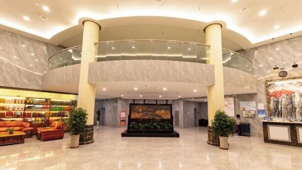 A spacious lobby with a marble floor, a reception desk, a seating area with sofas, and a large painting on the wall. - longdeguojifandian (Longde)