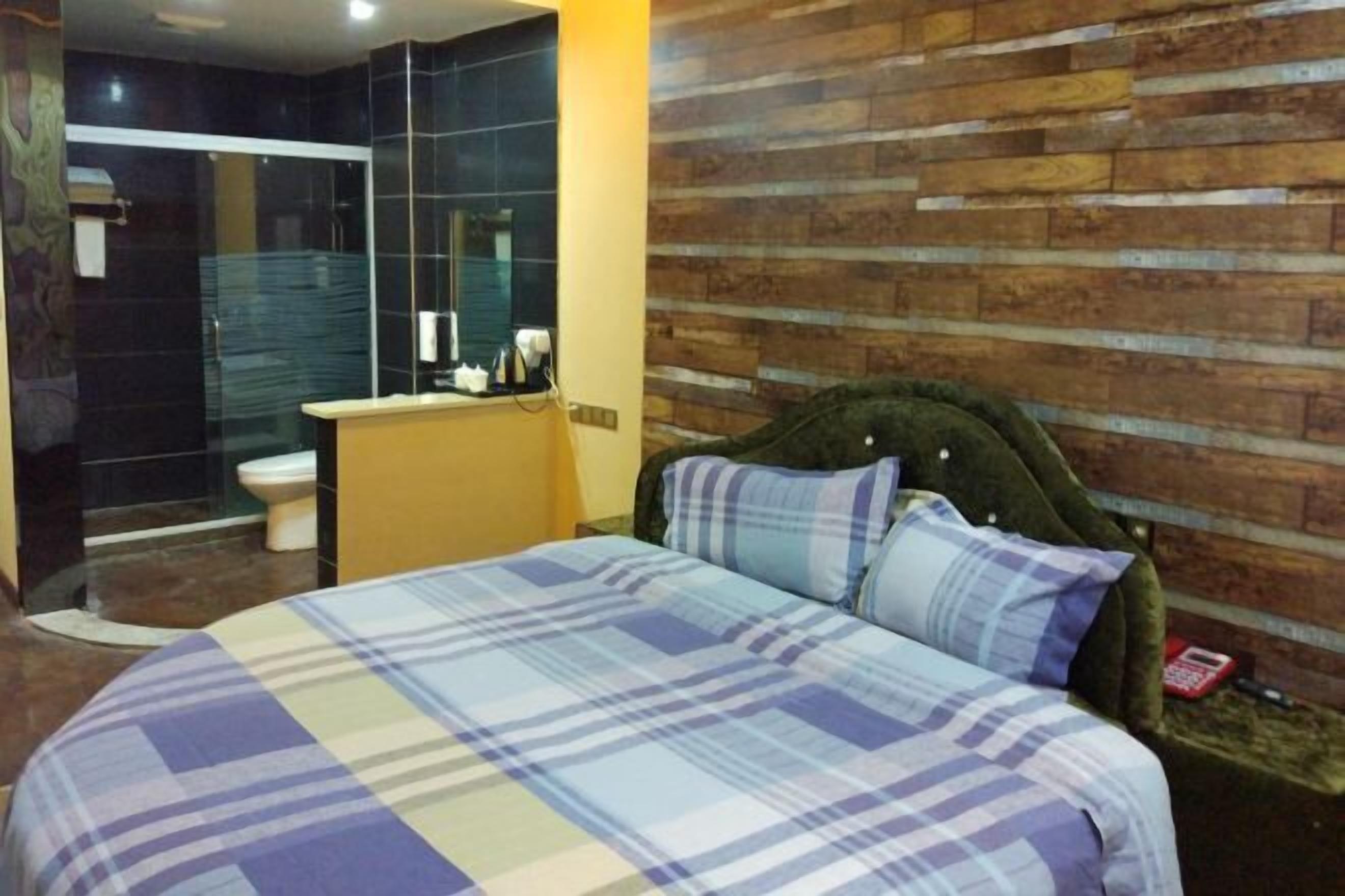 Un dormitorio con cama, cabecero de madera, baño con ducha de vidrio y lavamanos.