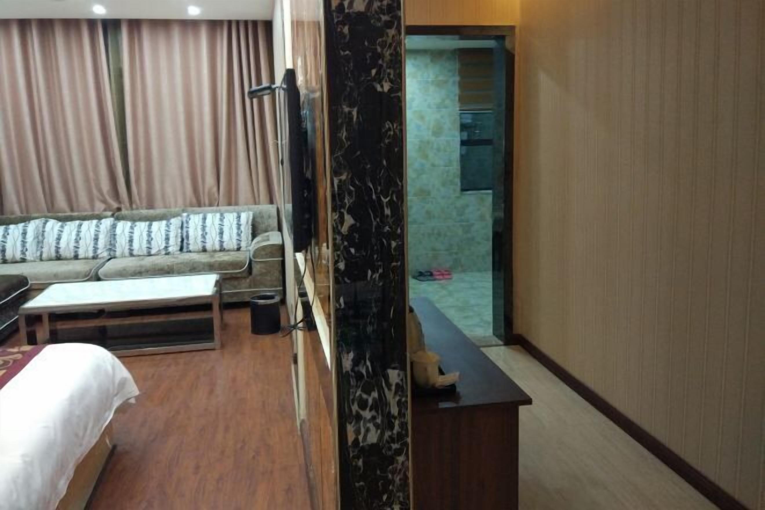 A hotel room with a sofa, a small table, a bed, a marble column, and a view of the bathroom.