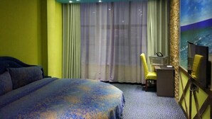Hotellihuone, jossa on sänky, työpöytä, tuoli ja suuri ikkuna, jossa on verhot.