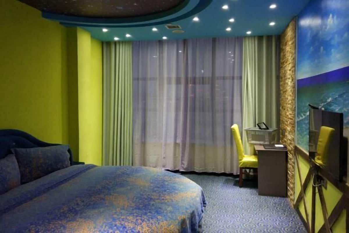 Una habitación de hotel con una cama, un escritorio, una silla y un ventanal con cortinas.