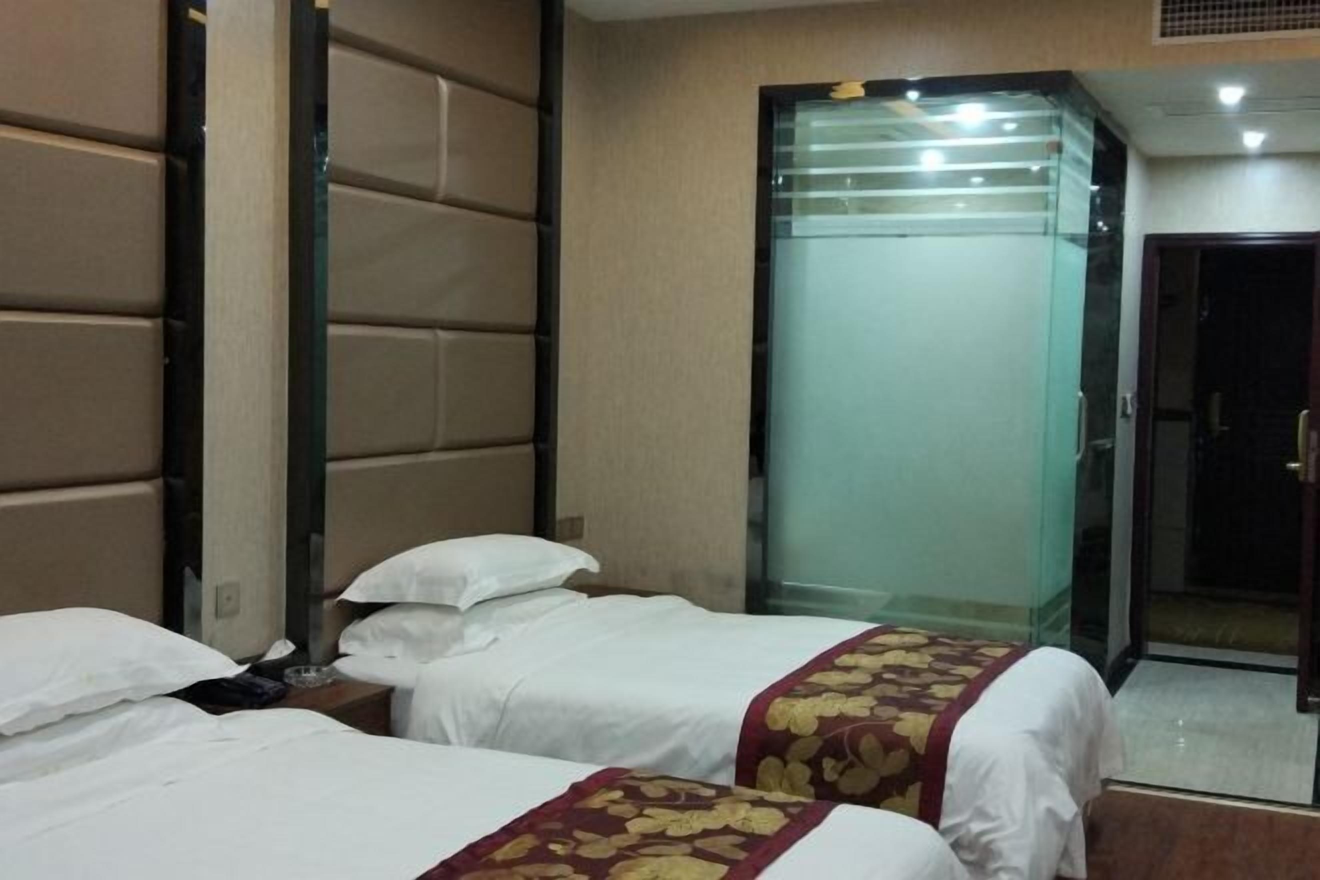 Ein Hotelzimmer mit zwei Betten, einer Glastrennwand und einer Tür zu einem Badezimmer.