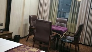 Hotellihuone, jossa on sänky, ruokapöytä tuoleineen, pieni pyöreä pöytä ja ikkuna, jossa on verhot.