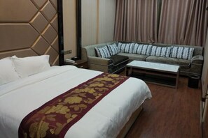 Una habitación de hotel con una cama grande, un sofá, una mesita y una cortina.