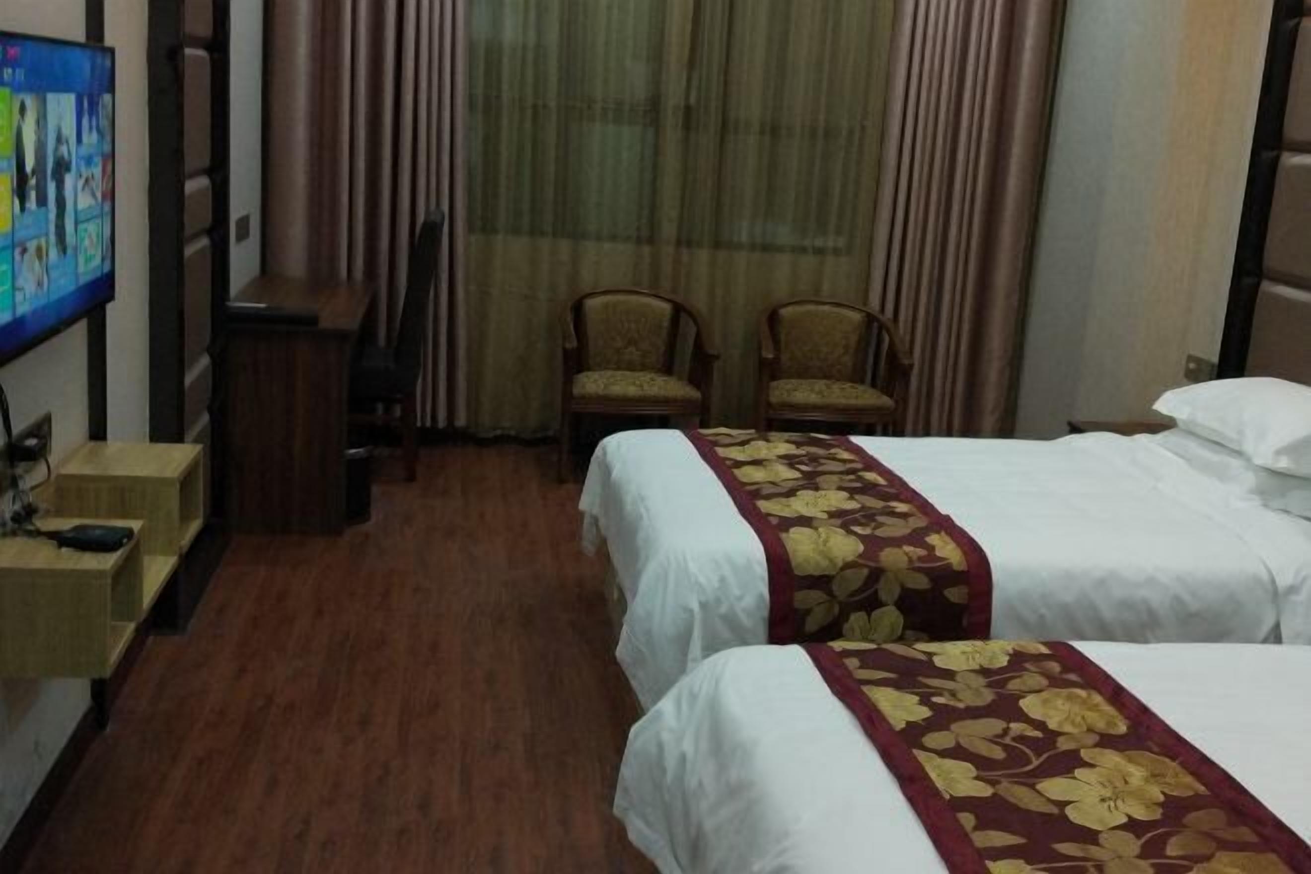 A hotel room with two beds, a television, a desk, and a chair.