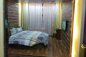 Ein Schlafzimmer mit Bett, Vorhängen, Fernseher und Holzboden.