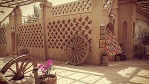 A courtyard with a patterned wall, a wooden cart, and a potted plant. - Anargvl Manor (Turpan)