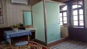 A room with a bed, a bedside table with a vase of flowers, a window with curtains, and a tiled floor. - Anargvl Manor (Turpan)