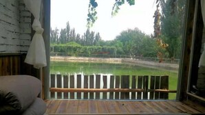 A room with a bed, a view of a pond, and a wooden deck outside. - Anargvl Manor (Turpan)