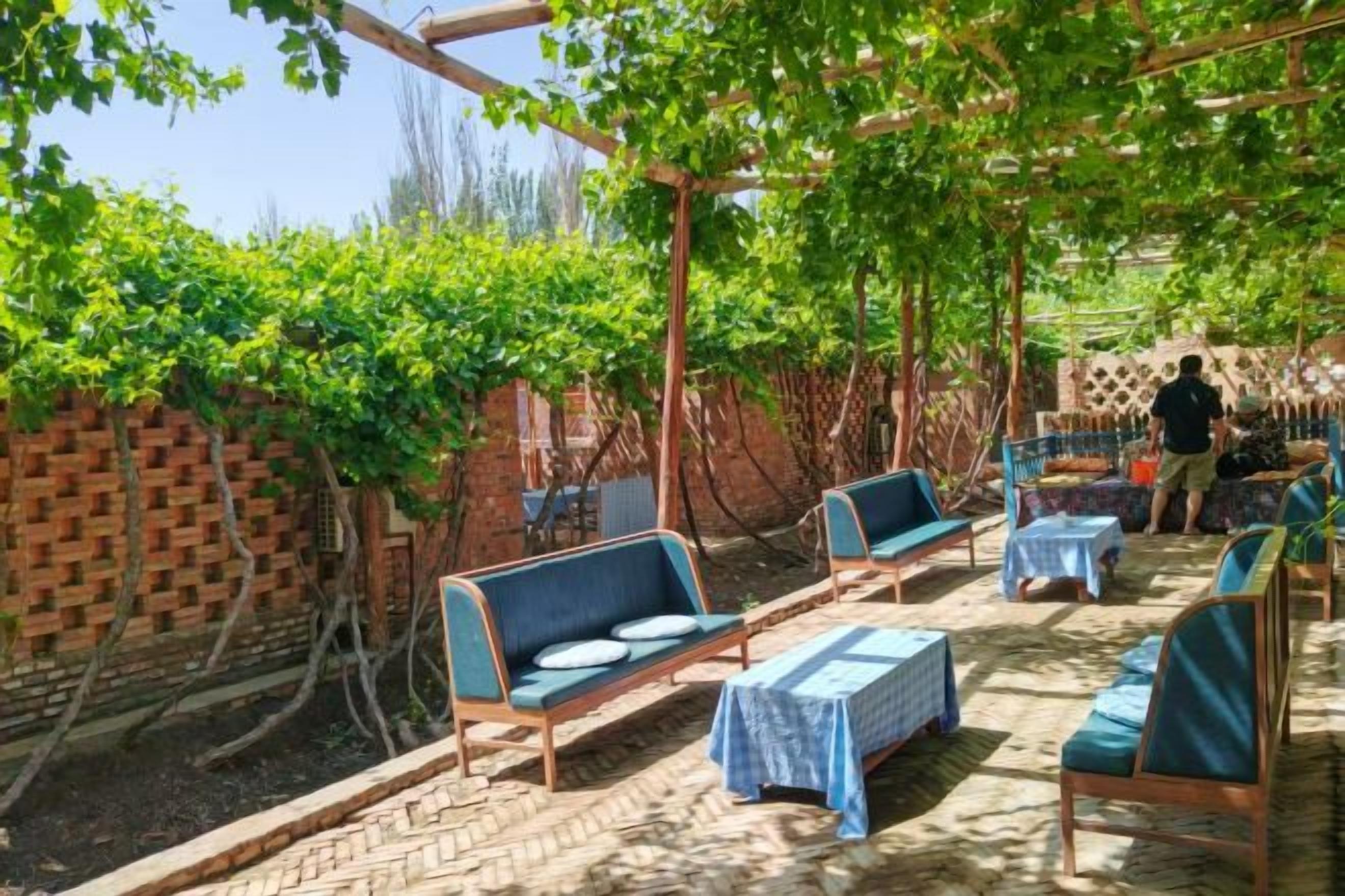 An outdoor seating area with tables and chairs, a brick wall, and a pergola with vines.