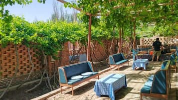 An outdoor seating area with tables and chairs, a brick wall, and a pergola with vines.