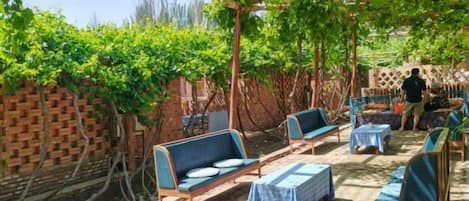 An outdoor seating area with tables and chairs, a brick wall, and a pergola with vines.