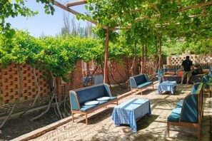 An outdoor seating area with tables and chairs, a brick wall, and a pergola with vines.