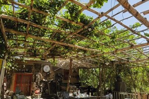 A rustic outdoor seating area with a wooden pergola, tables, chairs, and a rustic decor including a windmill and a large wheel. - Anargvl Manor (Turpan)