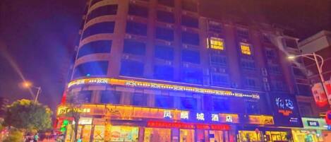 Un hotel de varios pisos con fachada curva, señalización iluminada y varios locales comerciales a nivel de calle.